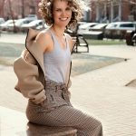 Cheerful woman with curly hair sitting outside in Kemerovo's sunny streets.